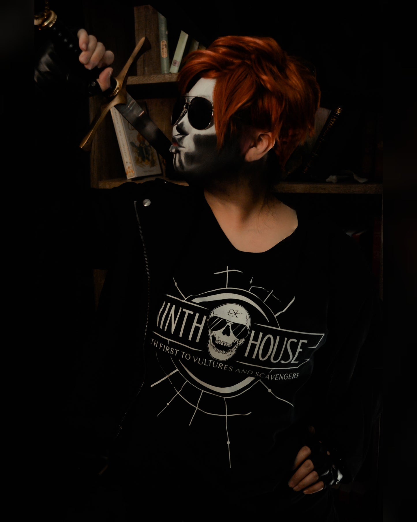 Gideon the ninth modeling the ninth house shirt in black with skull and the phrase "death first to vultures and scavengers" and holding a sword