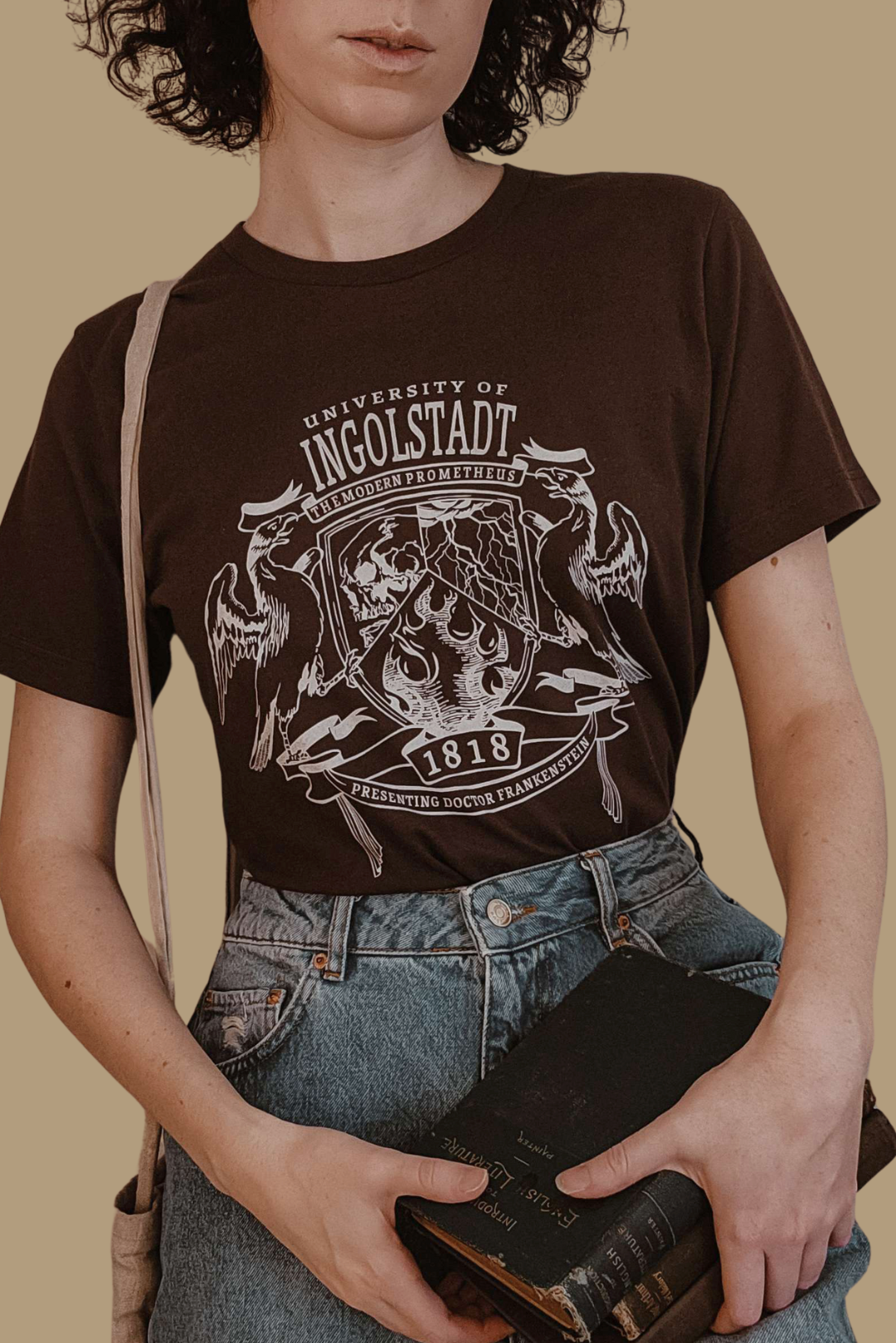 Person wearing a brown t-shirt with 'University of Ingolstadt' design, holding a book.
