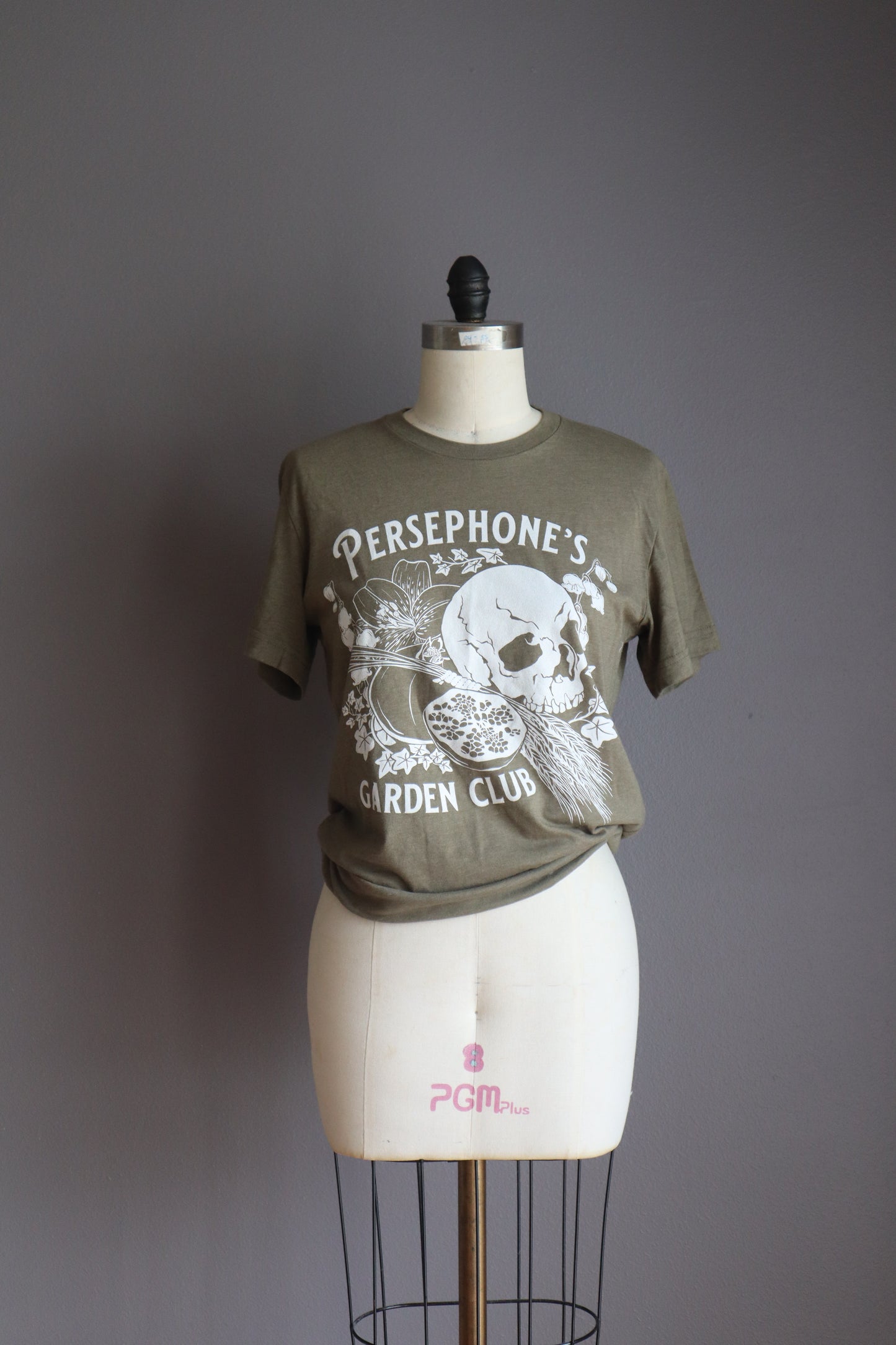 Persephone's Garden Club shirt in heathered olive with pomegranates and skull styled on a mannequin 