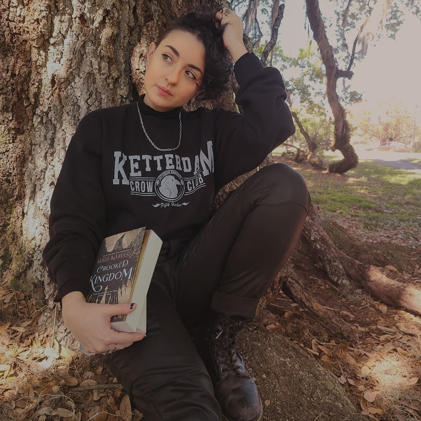 Ketterdam crow club university with crow logo sweatshirt worn by model leaning against tree