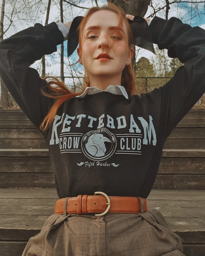 Ketterdam crow club university with crow logo sweatshirt worn by model in a dark academia style  