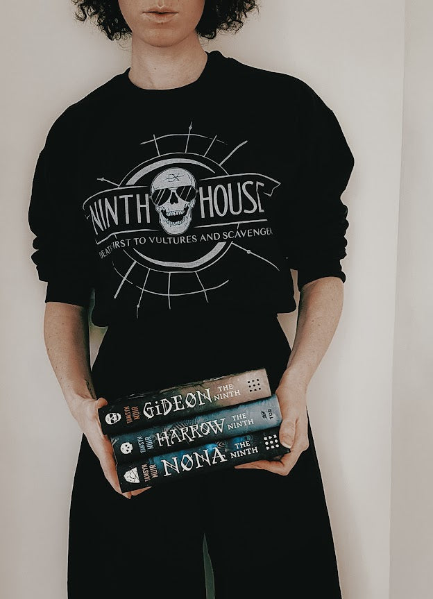Gideon the ninth themed ninth house sweatshirt in black with skull and the phrase "death first to vultures and scavengers" and three of the books from the series 