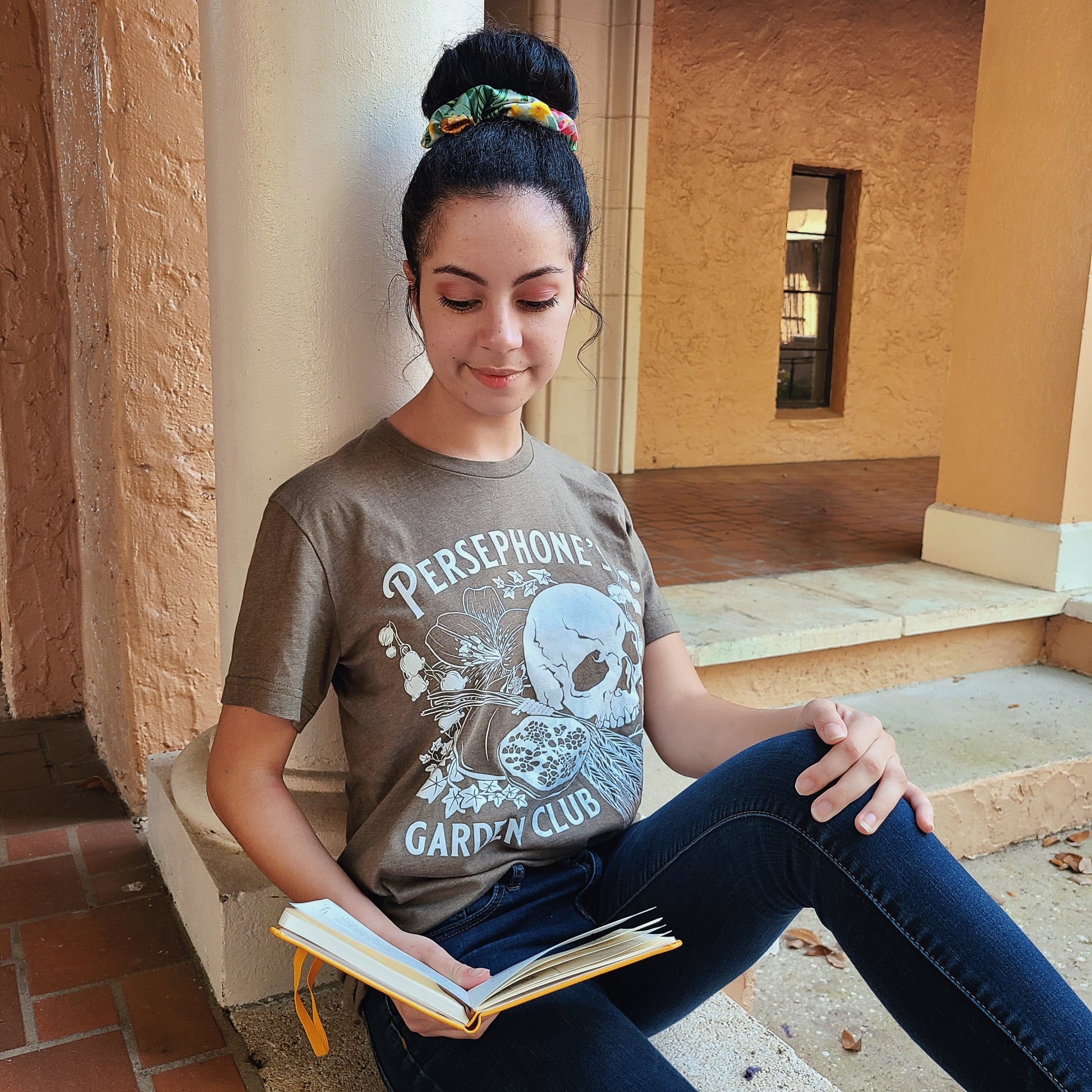 Persephone's Garden Club shirt in heathered olive with pomegranates and skull, worn on a student at a college campus