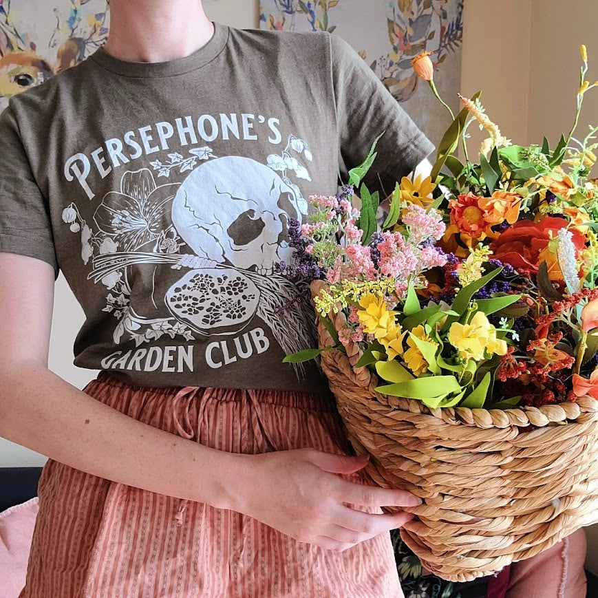 Persephone's Garden Club shirt in heathered olive styled with a basked of flowers like Persephone in the hades game 
