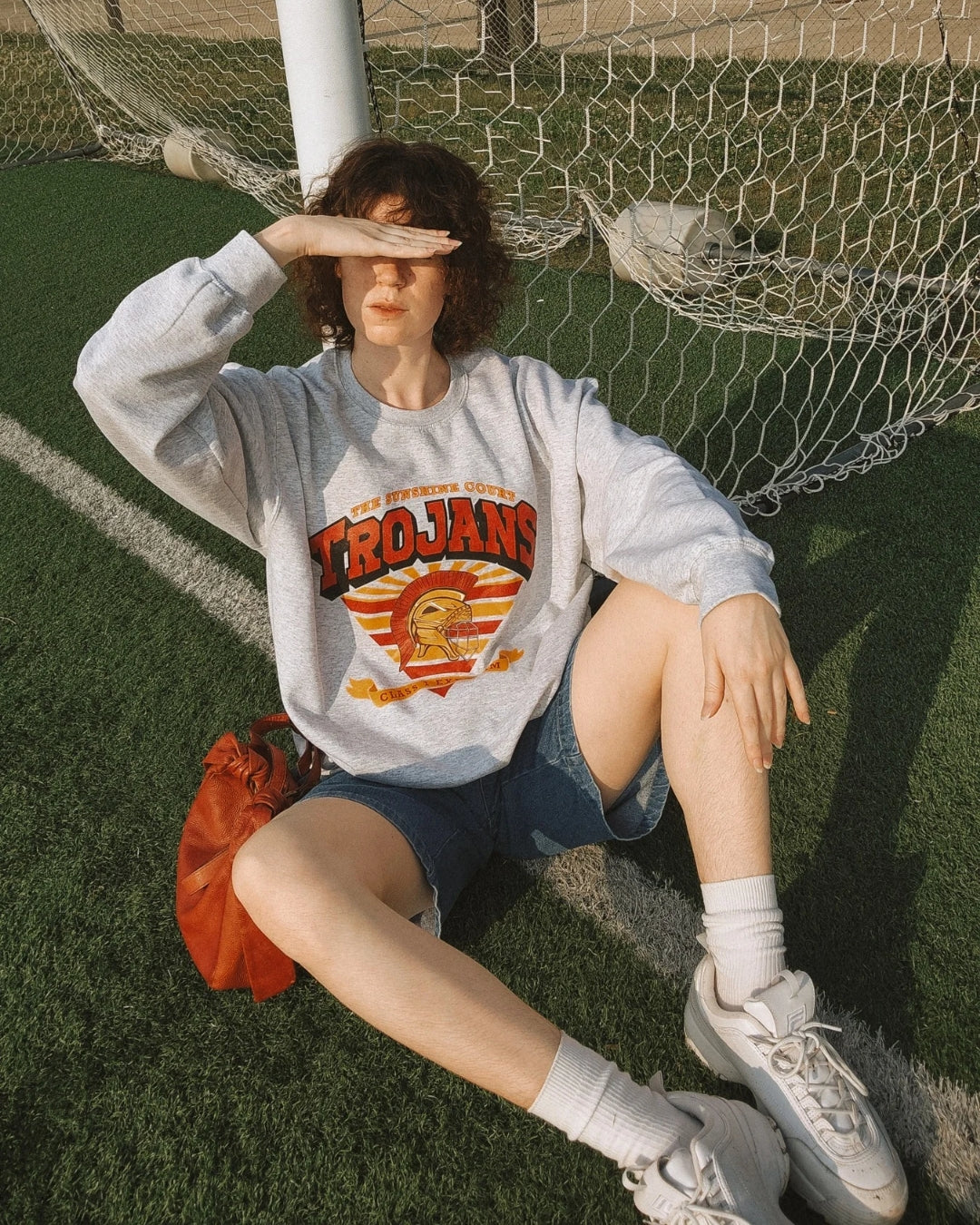 Trojan Sunshine Court Sweatshirt in Grey on model sitting on a soccer field